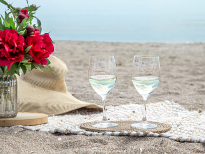 Twee glazen wijn en bloemen op het strand.