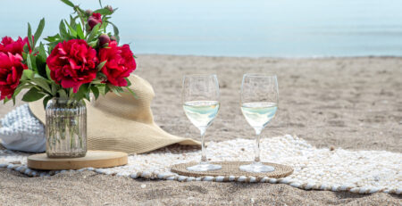 Twee glazen wijn en bloemen op het strand.