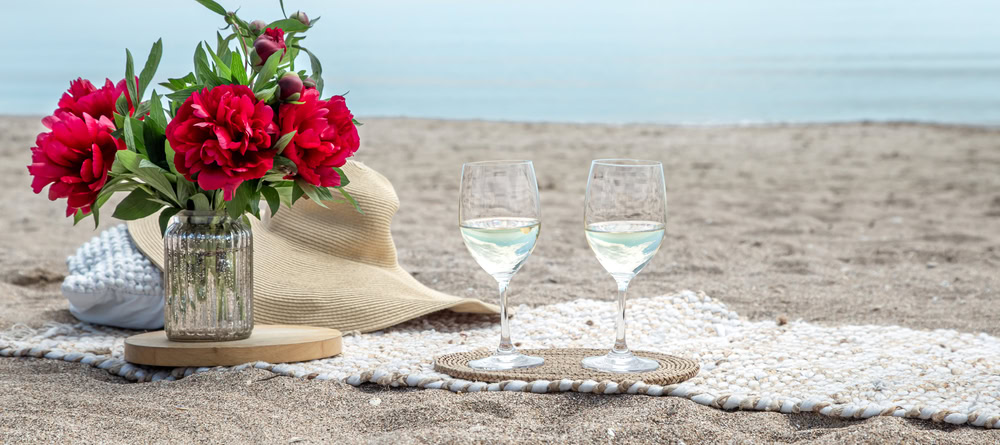 Twee glazen wijn en bloemen op het strand.